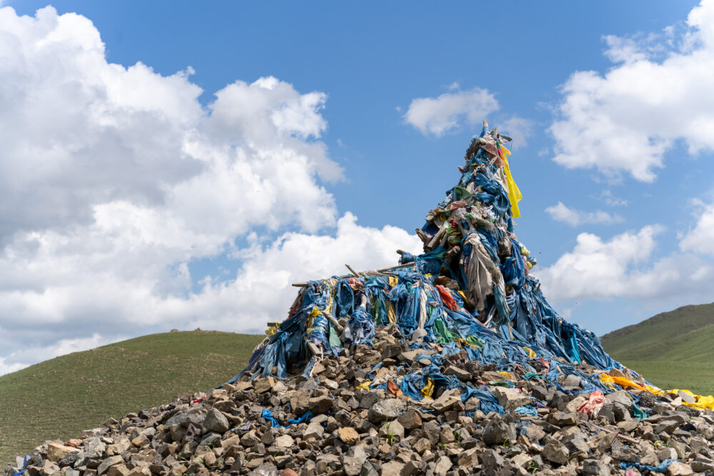stone pile on a hillside with blue ribbons tied to it. 