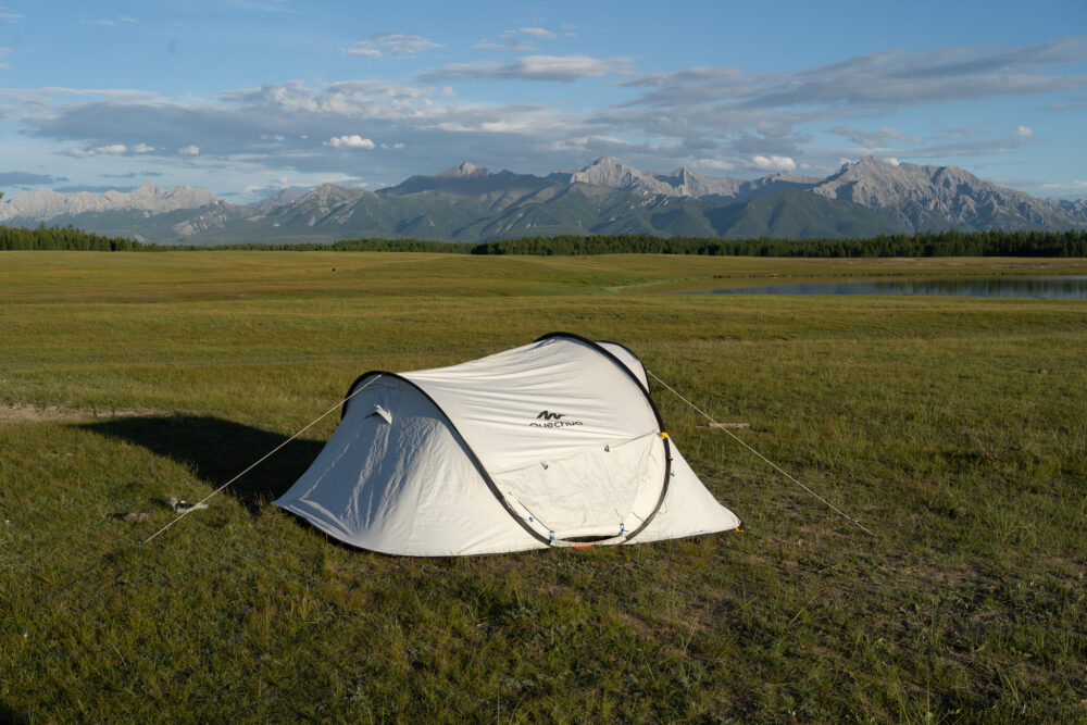 a white tent pitched in a grassy field with mountains behind. 