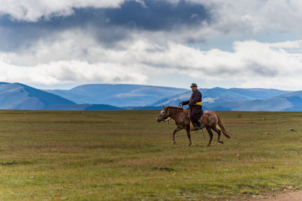 a mongolian man wearing traditional dress on top of his horse in the vast tundra 