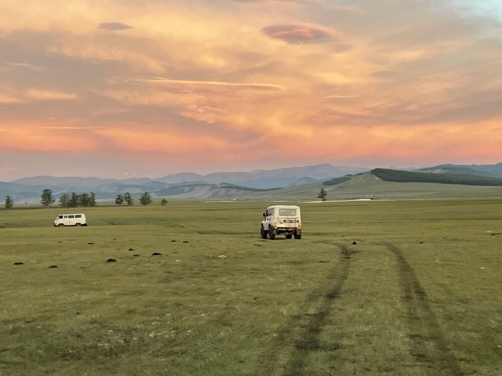 two vans riding across the green tundra into a pink sunset. 