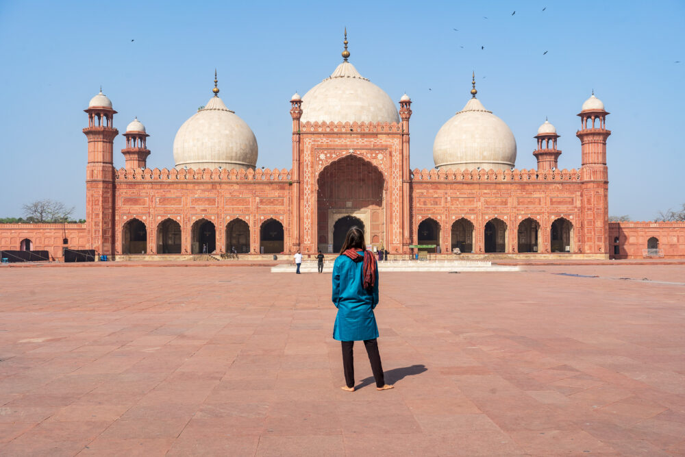 Evan in a blue traditional outfit in front of a large red mosque in lahore 