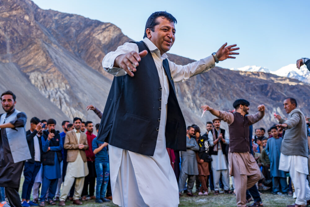 man dancing in a field in Pakistan with lots of other crowded around 