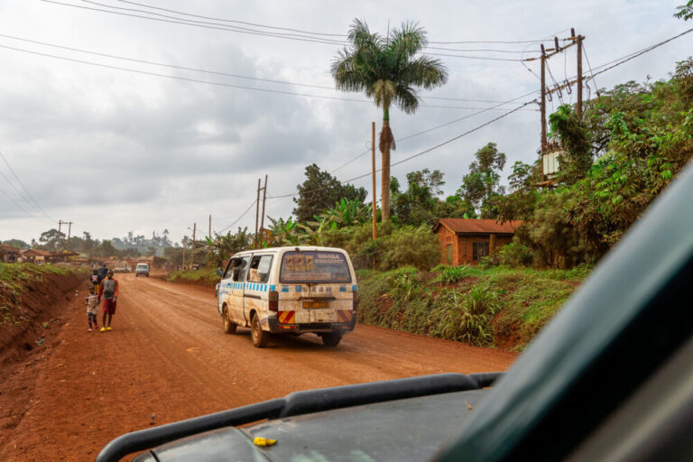 A van drives in front of us on a red clay road in Uganda