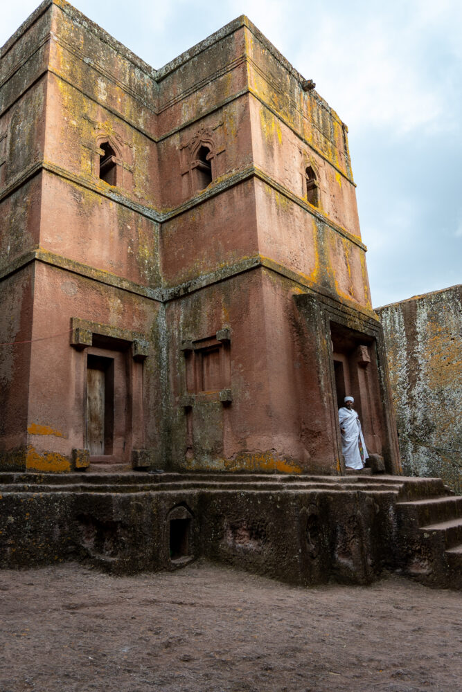 a white robed man coming out of one of the red rock churches in Lalibela