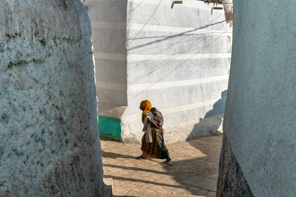 a woman carrying her child in the stucco walled city of Harar