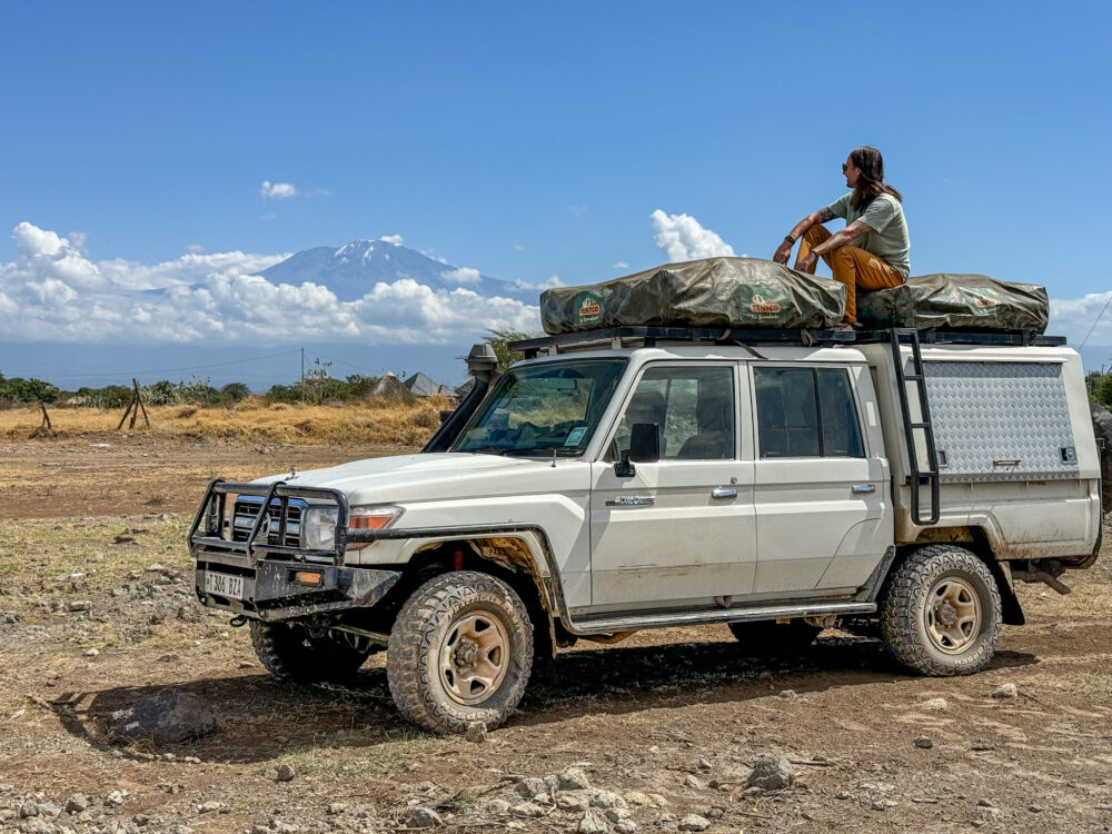 Evan sitting on top of a white landcruiser with mt kili in the background