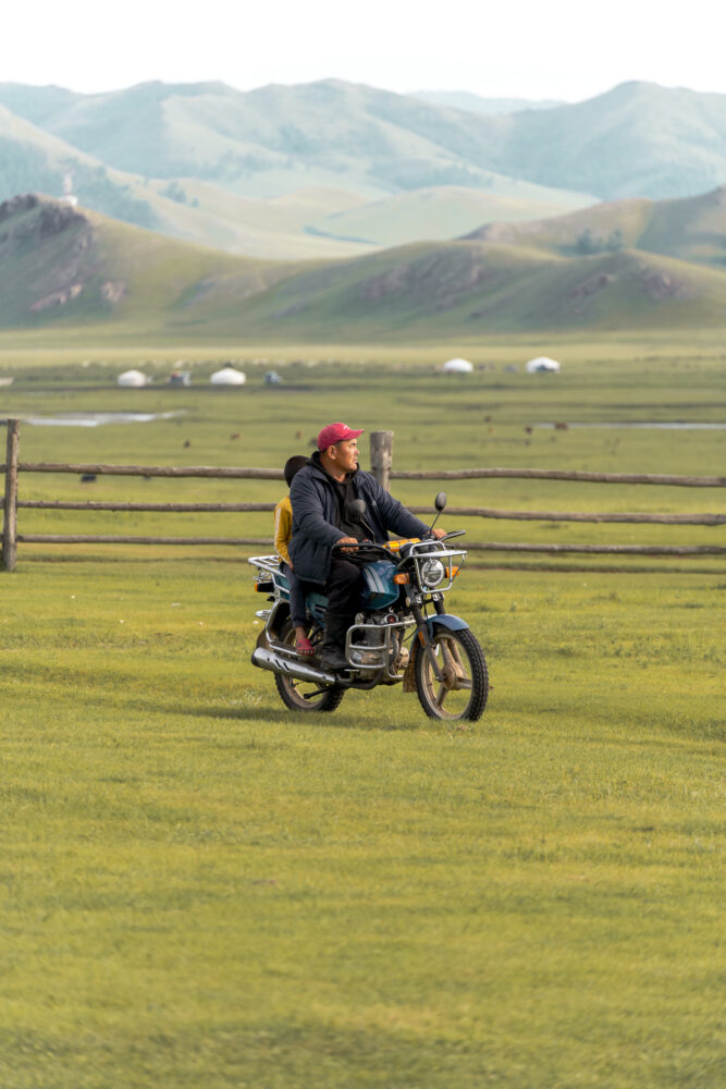 a mongolian man riding a motorcycle through the steppe