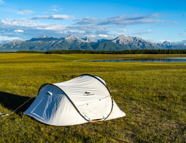 a white tent in a field with mountains in the distance and a lake