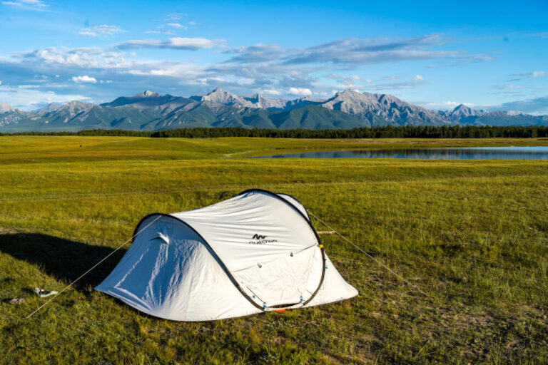a white tent in a field with mountains in the distance and a lake