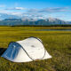 a white tent in a field with mountains in the distance and a lake