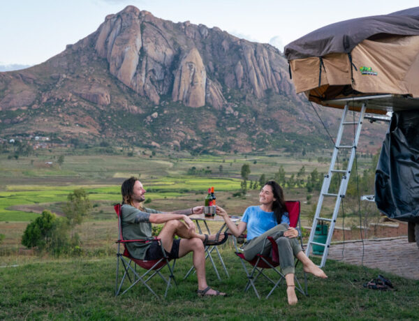 a couple drinking wine in camp chairs with car camper behind them