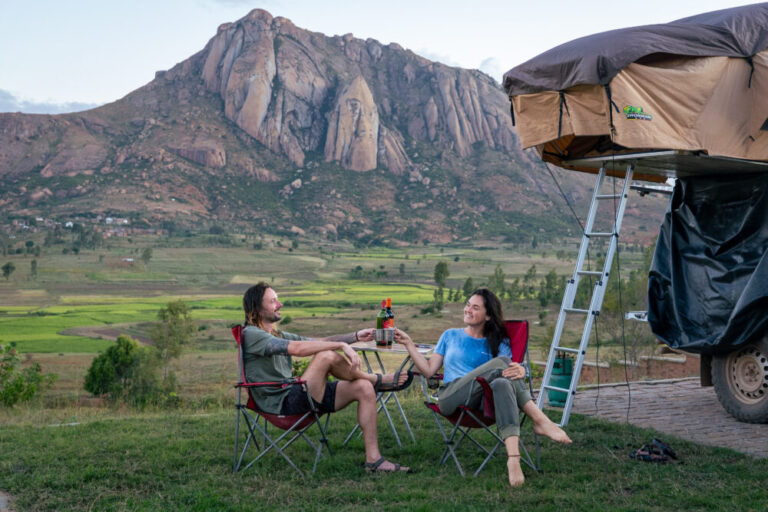 a couple drinking wine in camp chairs with car camper behind them