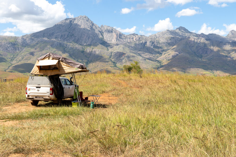 our rooftop tent and 4x4 parked in a grassy field overlooking a mountain view.