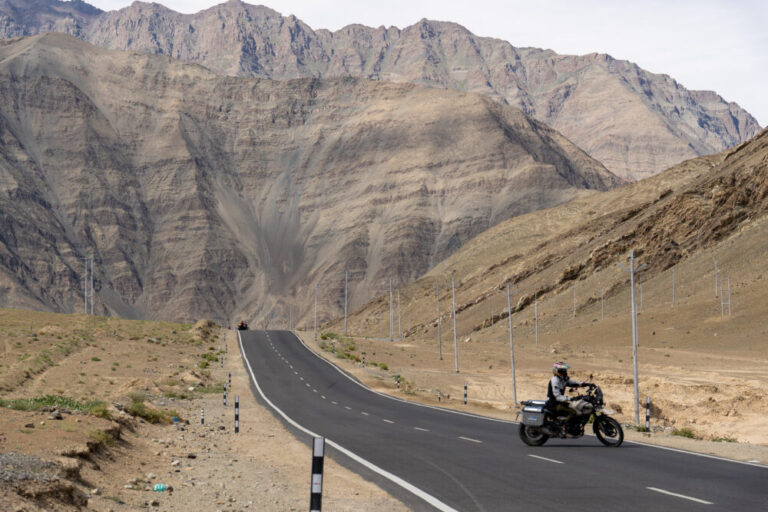 Man riding motorcycle on an asphalt road with a large mountain behind him