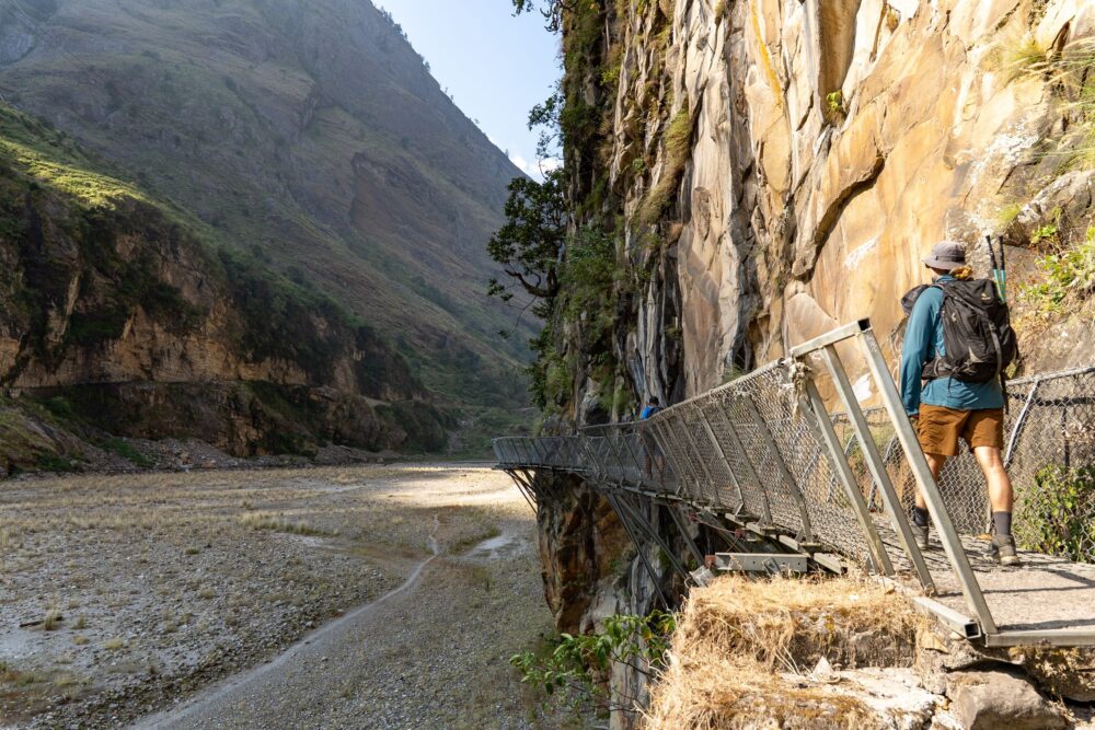 Evan walking on a hanging metal bridge on the Manaslu trail