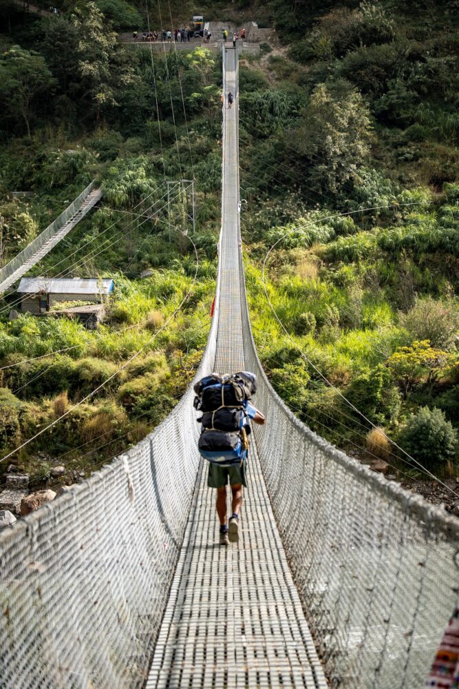 porter carrying our bags on a swinging suspension bridge