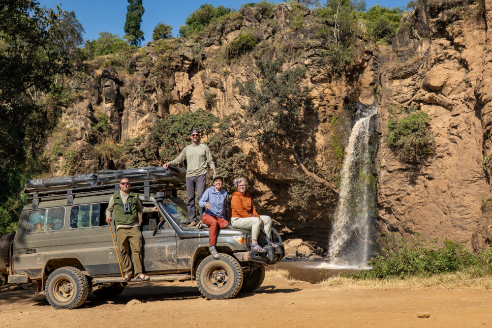 my family sitting on our car in front of a waterfall 